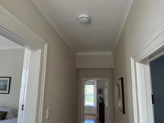 Ceiling smoke alarm in a narrow hallway with ornate trim and doorways in Paddington